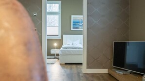 Een slaapkamer met een bed, nachtkastje, lamp, televisie en een raam met jaloezieën.