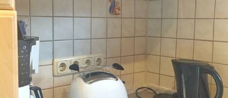 A kitchen with a white toaster, a black coffee maker, and a shelf with a bottle and a box.