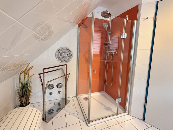 A modern shower enclosure with glass doors, a handheld showerhead, and a wall-mounted faucet.