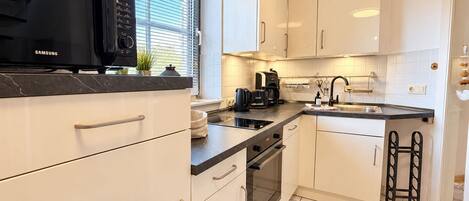 A modern kitchen with white cabinets, a black countertop, a built-in oven, and a window with blinds.