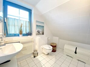 A bathroom with a white sink, a toilet, a radiator, and a window with blue curtains.