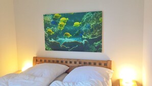 Une chambre avec un lit, une table de chevet et un tableau représentant des poissons dans un décor sous-marin, accroché au mur.