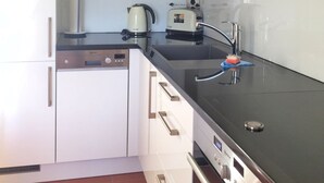 Une cuisine compacte avec des meubles blancs, un four à micro-ondes, une machine à café et un lave-vaisselle.