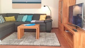 Un salon avec un canapé, une table basse, un téléviseur et un tableau représentant une scène de plage.