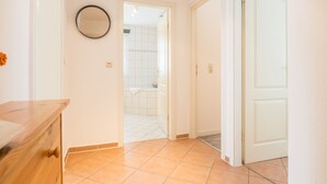 A hallway with a wooden bench, a round mirror, and a bathroom visible through an open door. - Ferienwohnung "naurulokki" (Baabe)