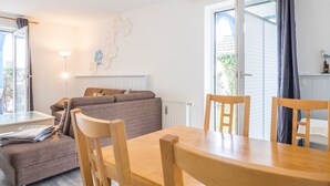 A modern living room with a sofa, a dining table with chairs, and a large window with curtains. - Ferienwohnung "naurulokki" (Baabe)