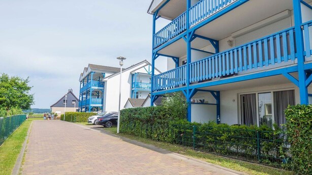 A row of modern, two-story buildings with blue balconies and a paved walkway. - Ferienwohnung "naurulokki" (Baabe)