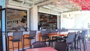 An outdoor seating area with tables and chairs, a bar with shelves of bottles, and a view of the street. - Ocean Sands Resort Oceanfront condo with Oceanfront Balcony! (Virginia Beach)