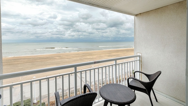 A balcony with wicker chairs overlooking a beach and ocean under a cloudy sky. - Ocean Sands Resort Oceanfront condo with Oceanfront Balcony! (Virginia Beach)