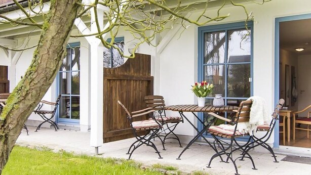 En udendørs terrasse med et bord, stole, et træhegn og en potteplante.