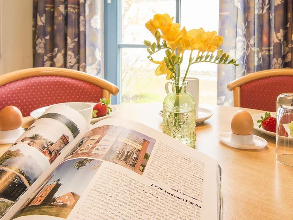 A dining table with a book open, a vase with yellow flowers, and a glass of water.