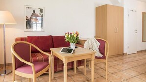 Et værelse med en rød sofa, et træbord med en tablet, en gulvlampe og en træskab.