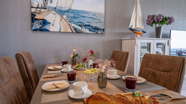 A dining table with a sailboat painting, a small sailboat model, and a vase with flowers.