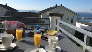 A breakfast setup on a balcony with a view of the sea, including a basket, juice, and breakfast items.