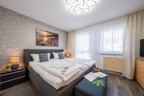 Ein modernes Schlafzimmer mit Bett, Nachttischen, einem Fenster mit Vorhängen, einer Heizung und einem an der Wand befestigten Fernseher.