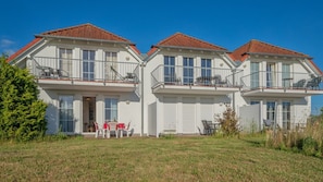 A two-story residential building with a red-tiled roof, white exterior walls, and balconies with metal railings.