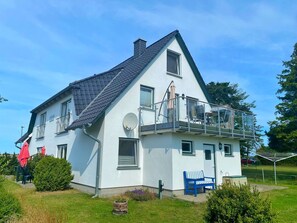 Et tosidet hus med balkon, parabanolantenne og en lille have.