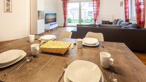 A dining area with a wooden table set for four, a wicker basket, and a sofa in the background.