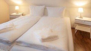 A twin bed with white linens and pillows, two bedside tables with lamps, and a wooden floor.
