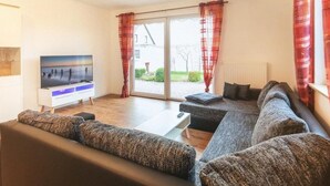 A modern living room with a large flat-screen TV, a sofa set, and a dining table.