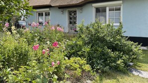 A house with a thatched roof, a front porch, and a garden with pink flowers. - Reethaus Vilmnitz - Ferienwohnung "vilm" - Reethaus Vilmnitz (Putbus)
