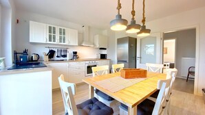 Une cuisine moderne avec des meubles blancs, un îlot central et un coin repas comprenant une table en bois et des chaises blanches.