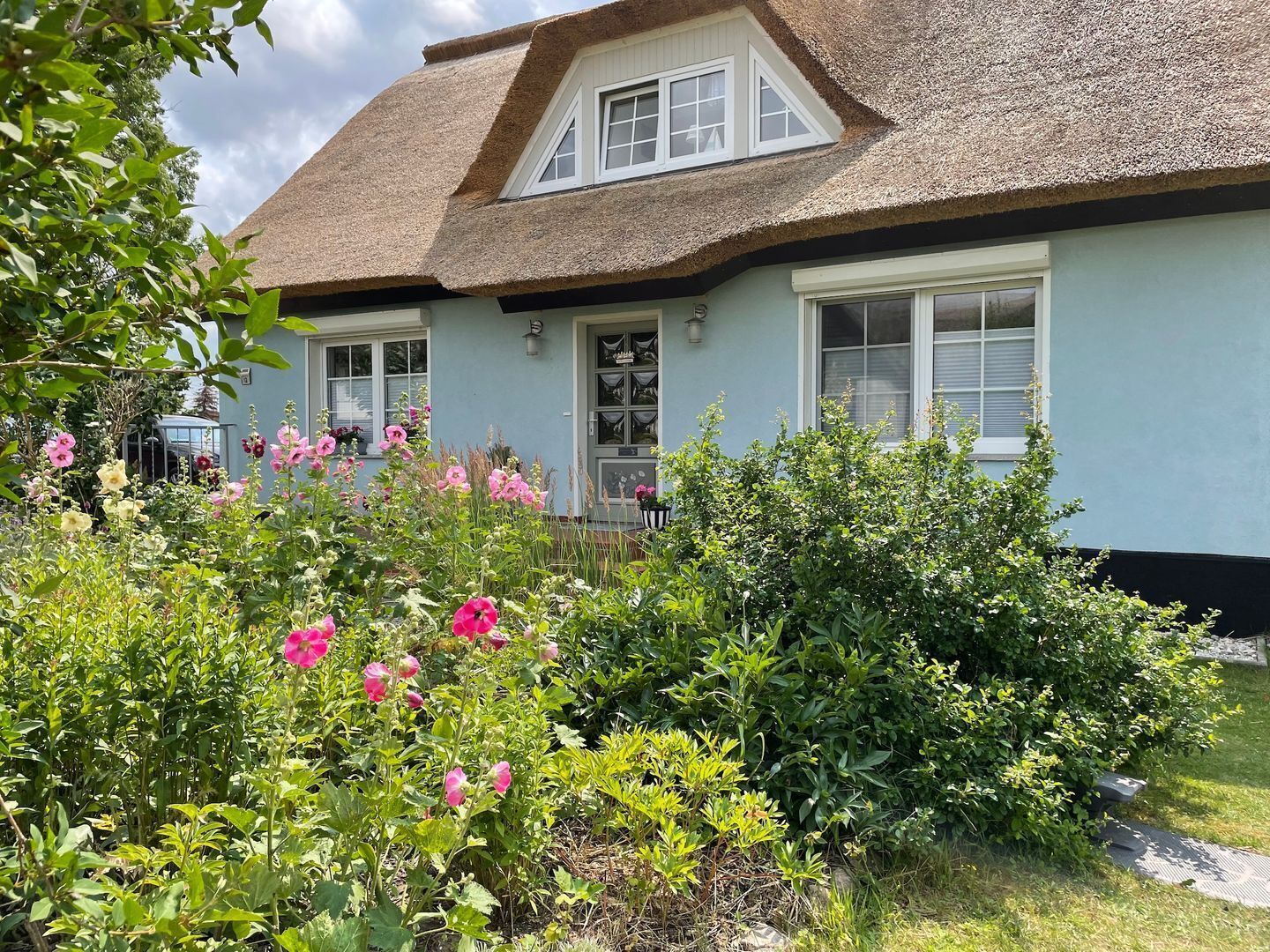 Ein Haus mit einem Strohdach, hellblauer Fassade und einem Garten mit rosa Blüten.