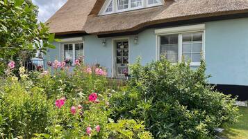Ein Haus mit einem Strohdach, hellblauer Fassade und einem Garten mit rosa Blüten.