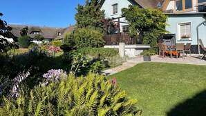 Une maison traditionnelle à toiture de chaume, entourée d’un jardin bien entretenu où poussent diverses plantes et fleurs.