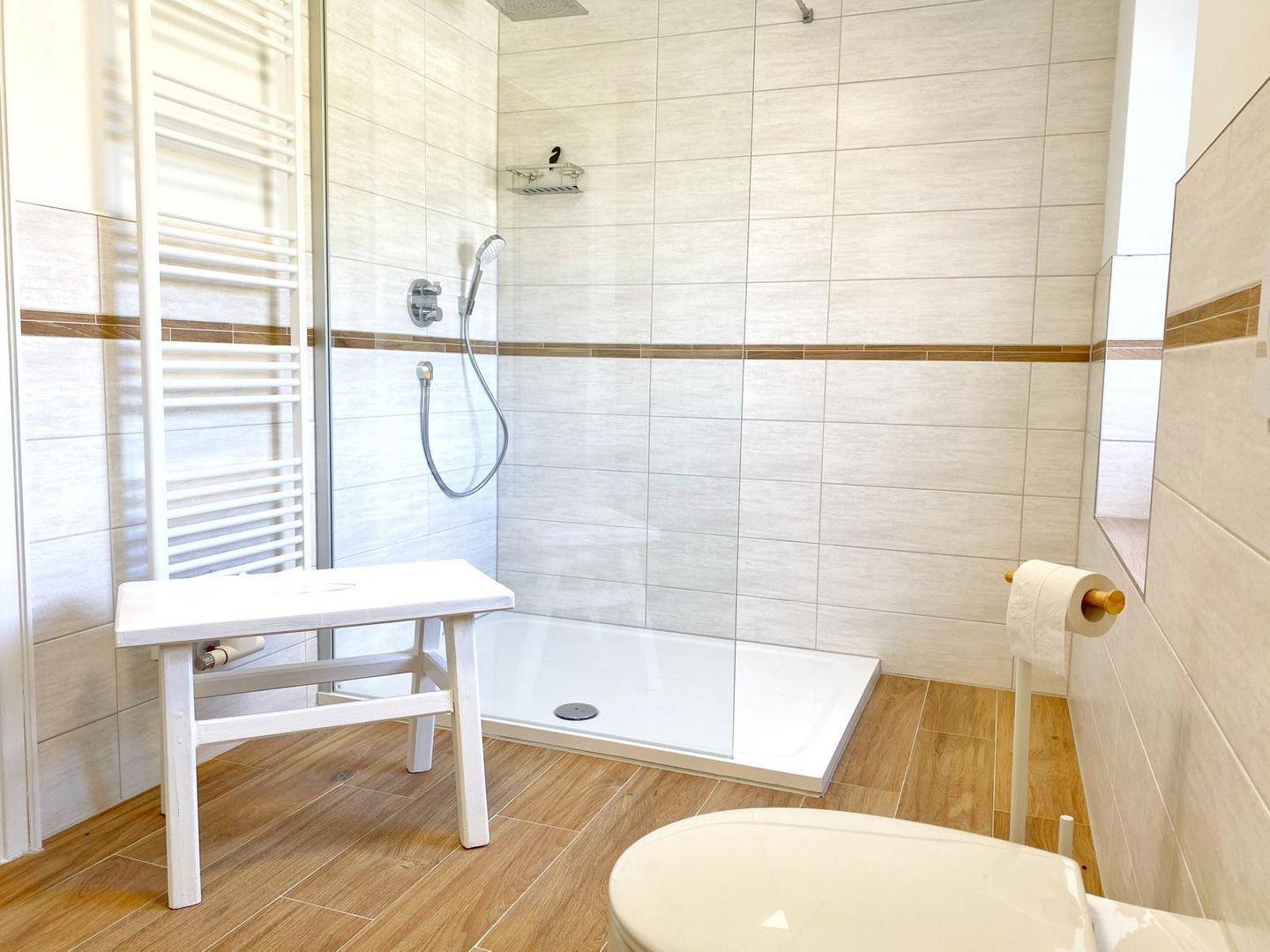 A modern bathroom with a shower, toilet, and a small bench.