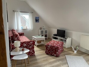 A cozy loft-style living room with a red floral sofa, a white coffee table, a small white cabinet, and a television on a white stand.