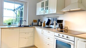 Een moderne keuken met witte kastjes, een ingebouwde oven, een koffiezetapparaat en een raam dat natuurlijk licht biedt.