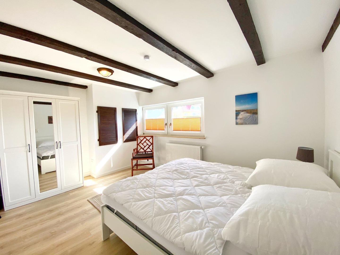 Ein Schlafzimmer mit Bett, Fenster mit Jalousien, Heizkörper, Stuhl und Kleiderschrank.