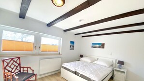 Een slaapkamer met een bed, een stoel, een radiator, een raam met zonwering en een plafondlamp.