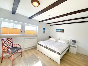 A bedroom with a bed, a chair, a radiator, a window with blinds, and a ceiling light.