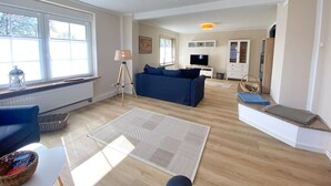 Een ruime woonkamer met een blauwe bank, een staande lamp en een televisie.