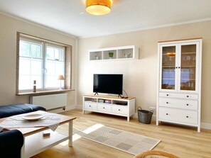 Een moderne woonkamer met een flatscreen televisie, een bank, een salontafel en een kast met glazen deuren.