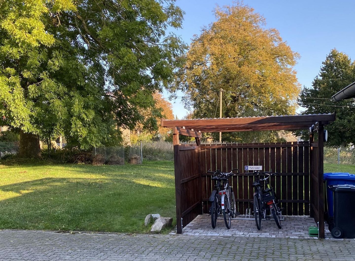 Ein überdachter Fahrradparkplatz mit Holzzaun, einem Schild für Radfahrer und einem Mülleimer.