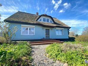 A house with a thatched roof, a front porch, and a gravel pathway leading to the entrance.