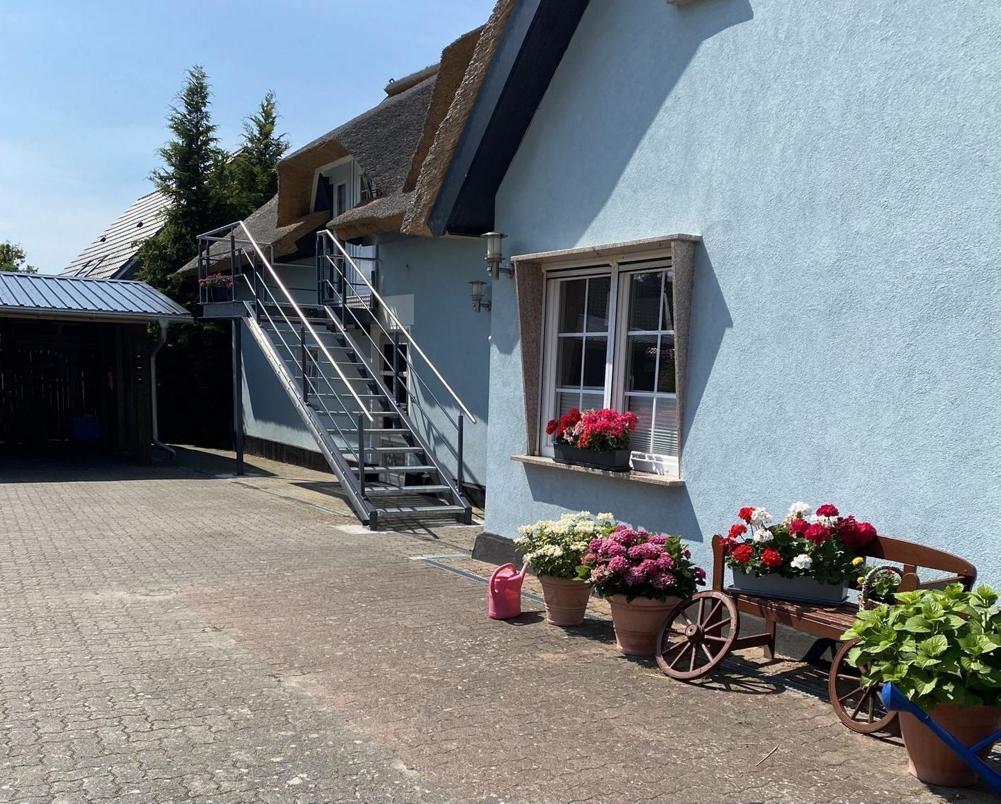 Ein Gebäude mit blauer Fassade, einer Treppe, die zu einem überdachten Bereich führt, und Blumentöpfen davor.
