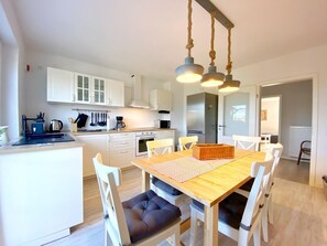 A modern kitchen with white cabinets, a central island, and a dining area with a wooden table and white chairs.