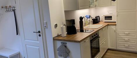 A compact kitchen with white cabinetry, a wooden countertop, a coffee maker, a microwave, and a built-in oven.