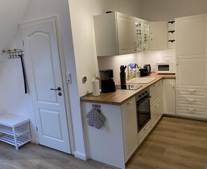 A compact kitchen with white cabinetry, a wooden countertop, a coffee maker, a microwave, and a built-in oven.
