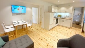 A modern apartment with a dining area, kitchenette, and a living room with a sofa and a TV displaying a map.