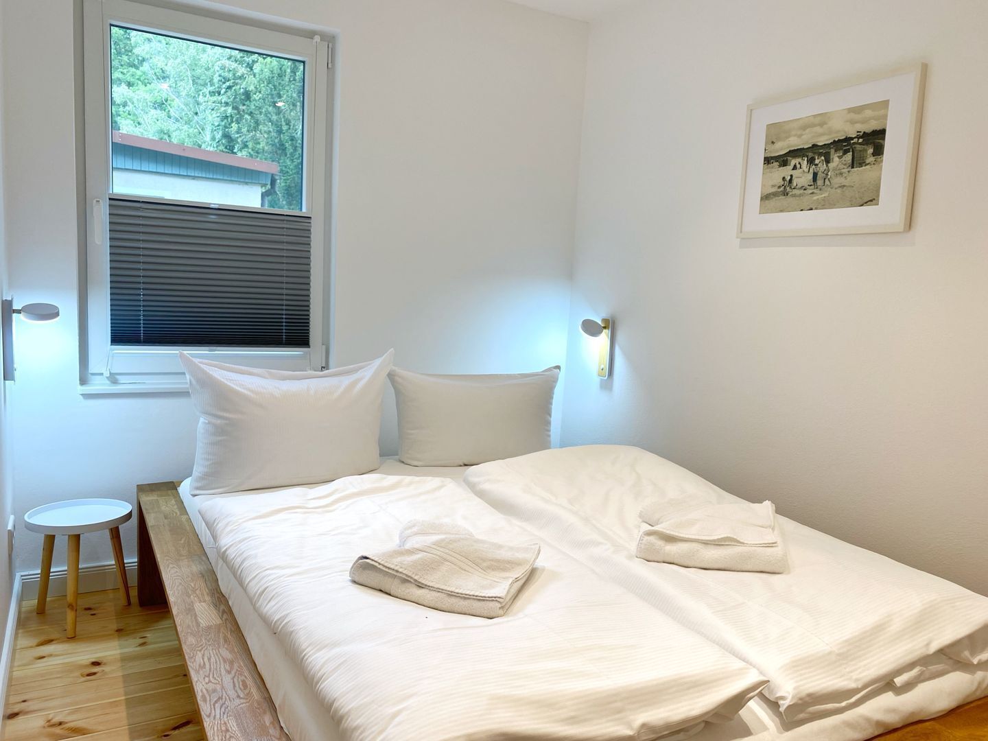 Un dormitorio con una cama individual, una mesita de noche pequeña, una ventana con persianas y una lámpara fijada a la pared.