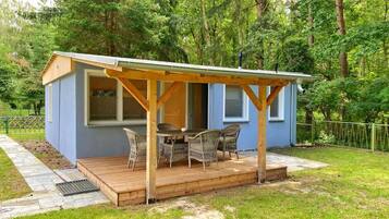 A small blue cabin with a wooden deck and wicker furniture.
