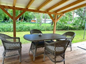 Eine überdachte Terrasse im Freien mit einem Tisch und vier Korbstühlen.