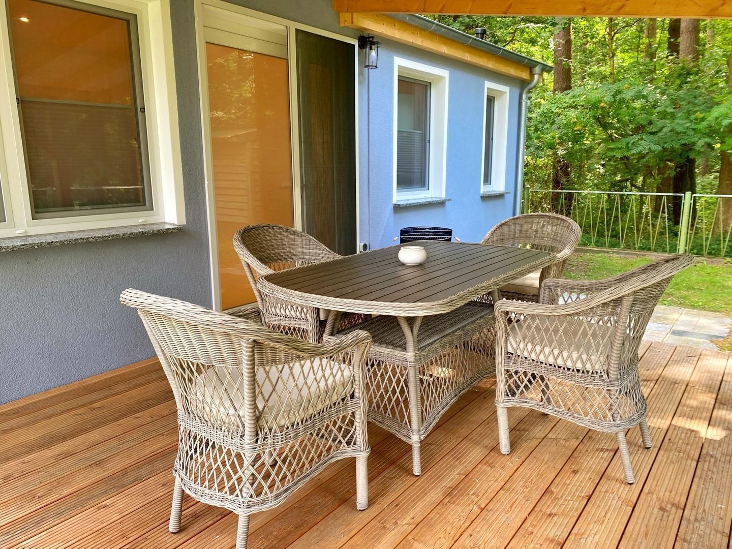 Une terrasse avec une table et des chaises en osier, une petite structure bleue et une plateforme en bois.