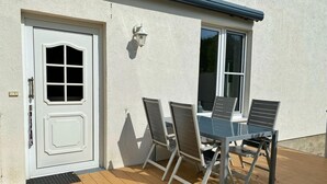 Un patio con una mesa, sillas, una puerta blanca y una ventana.