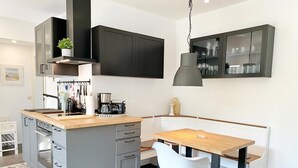 Una cocina moderna con armarios grises, encimera de madera y una zona de comedor con una silla y mesa blancos.